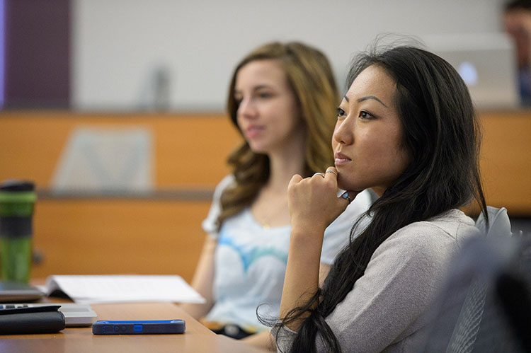  Two students sitting side by side at a desk listening to a lecture or presentation.