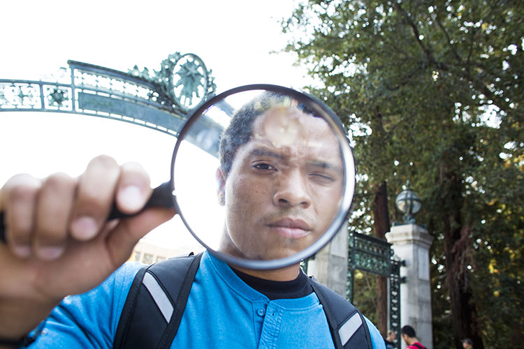 Student at Sather Gate looking through a magnifying glass. 