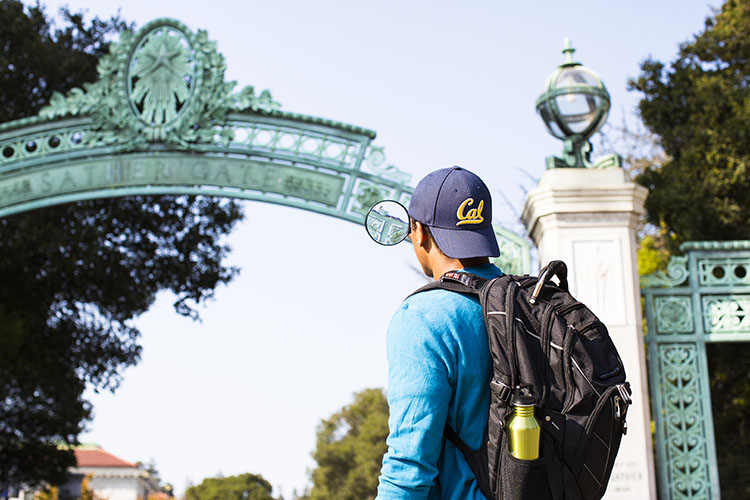  One student wearing a Cal cap with a backpack in front of Sather Gate.