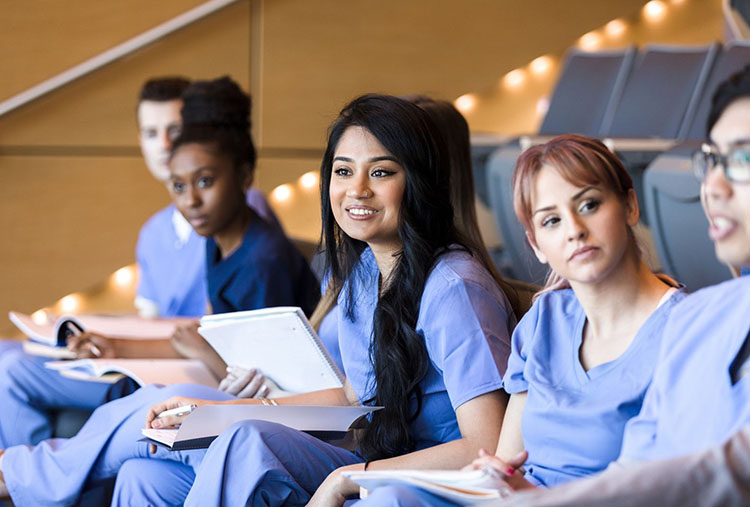  Six medical students in scrubs taking notes during a lecture.