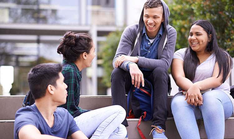  Four students sitting outside on stairs smiling.