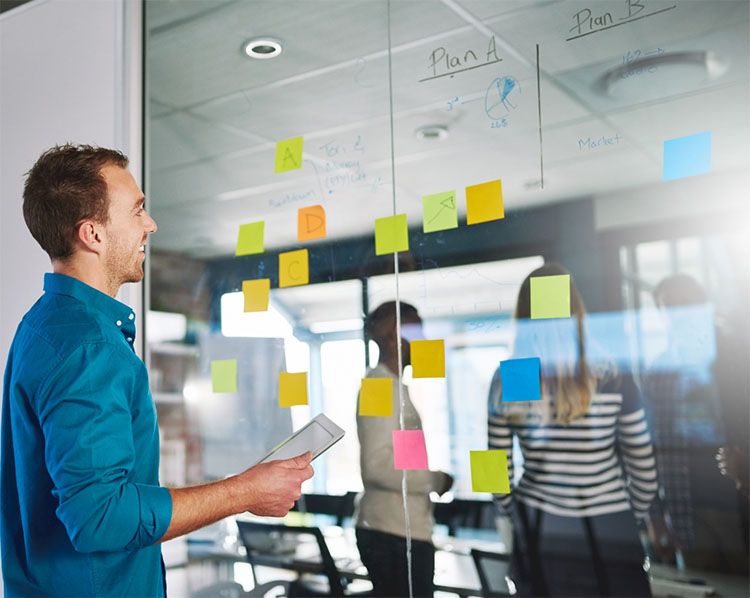  A man looking at a window with colorful sticky notes and two people on the other side of the window.