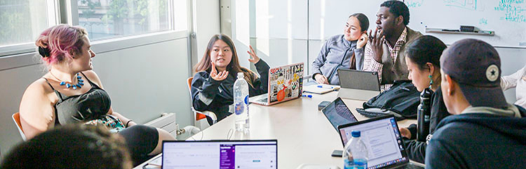  Seven students sit in front of their laptops around a conference table, engaged in robust discussion.